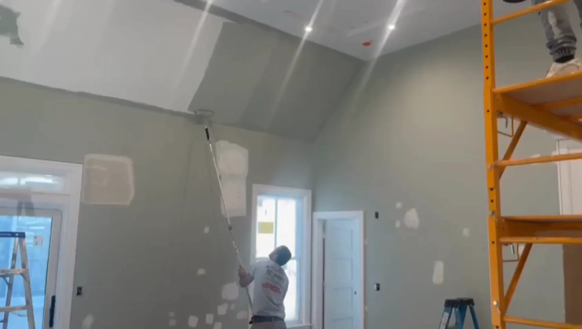 Interior painting project with worker rolling paint on high walls.