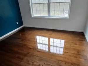 Newly refinished wood floor in a room with blue wall, reflecting light.