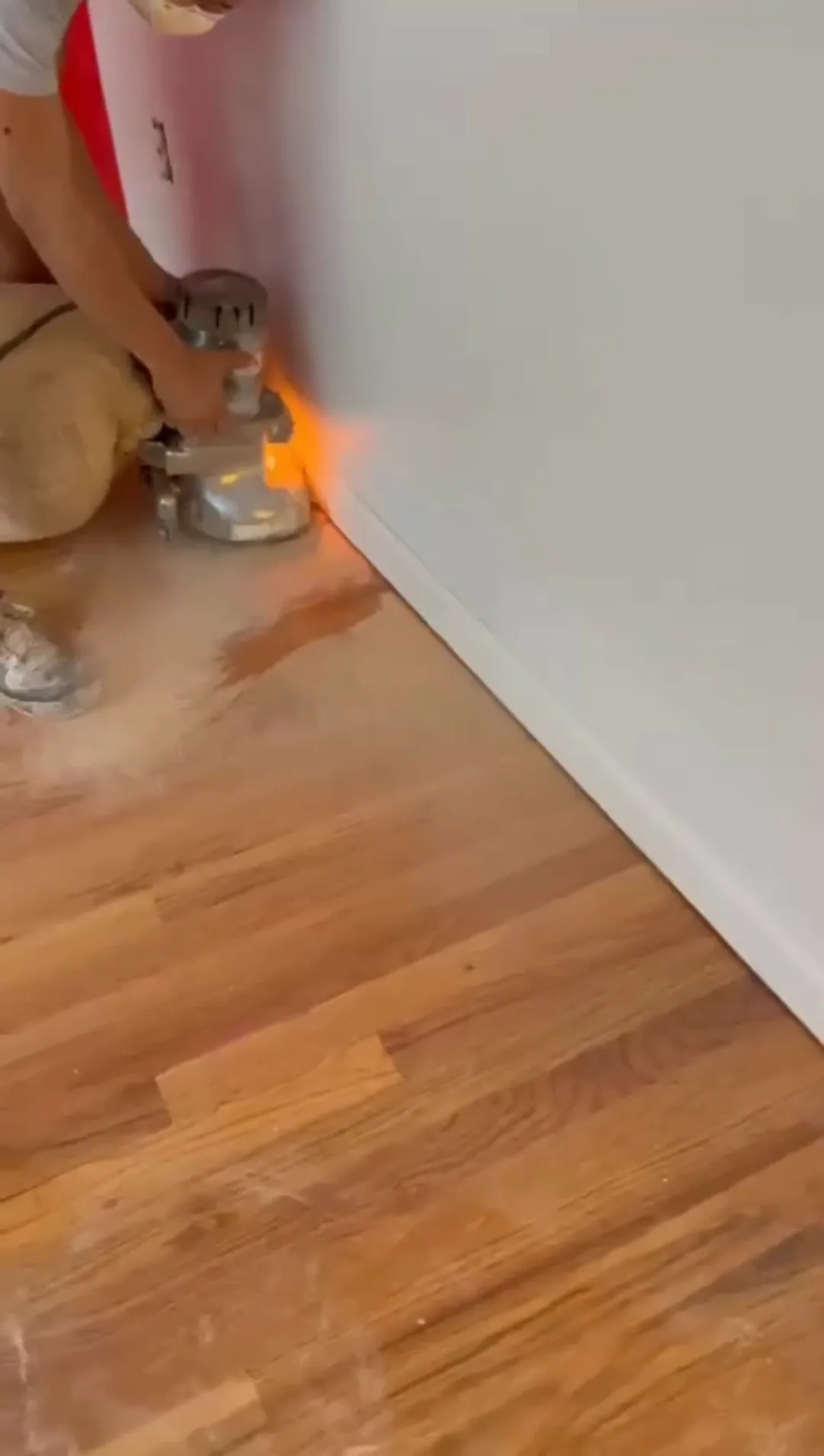 Wood floor refinishing work in progress, sanding and finishing near wall.