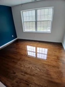 Newly refinished wood floor in a room with blue wall, reflecting light.