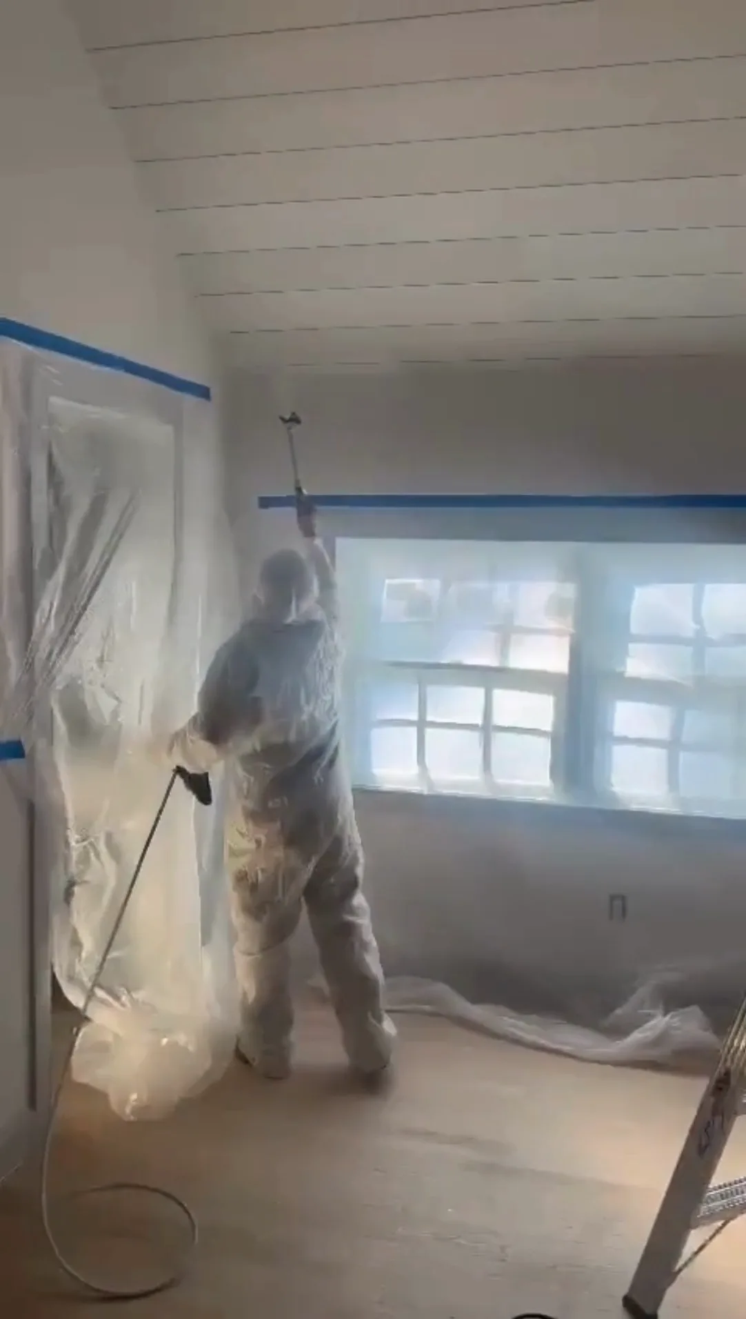 Professional spraying paint on ceiling during hardwood floor refinishing.