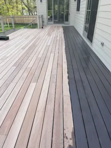 View of deck staining in progress, showing a sharp contrast between the dark stained section and the natural wood.