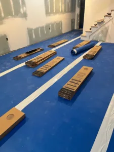 Overview of a basement room prepped with blue protective film and multiple staged boxes of flooring for a comprehensive composite vinyl plank installation.