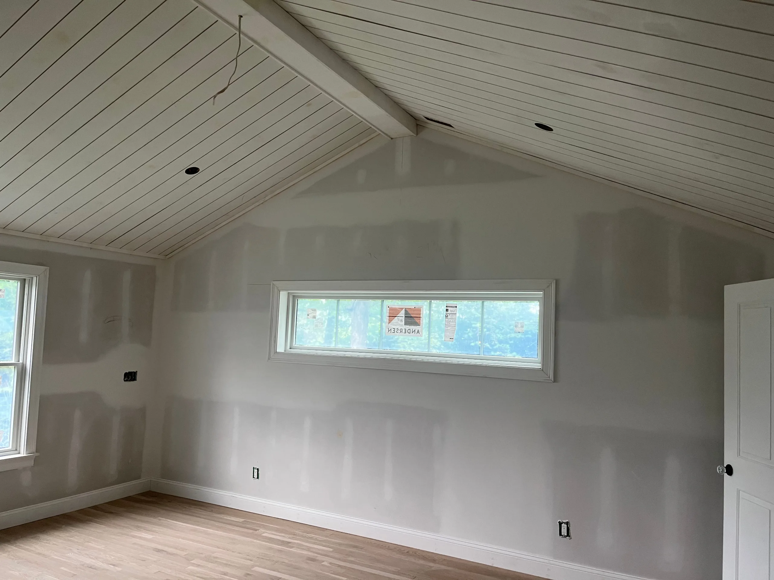 Wide-angle view of a vaulted room showing the smooth, seamless drywall finish around windows and a door opening, prepped for paint.