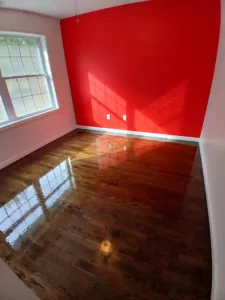 Shiny dark hardwood flooring reflecting a large window in a room with an accent red wall.