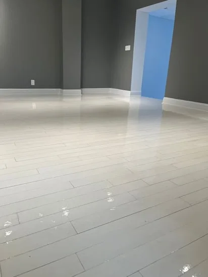 Another perspective of a glossy white hardwood floor refinishing next to a stair step, with the white walls and trim visible.