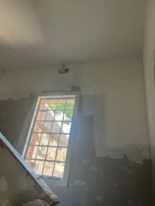 Ceiling water damage restoration showing prepped walls and fresh primer around a window.