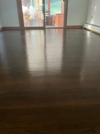 Hardwood floor refinishing viewed toward a sliding glass door to demonstrate surface reflection and evenness.