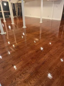 The completed hardwood floor refinishing process, displaying a newly applied dark stain and a high-gloss protective topcoat reflecting the room's lighting.
